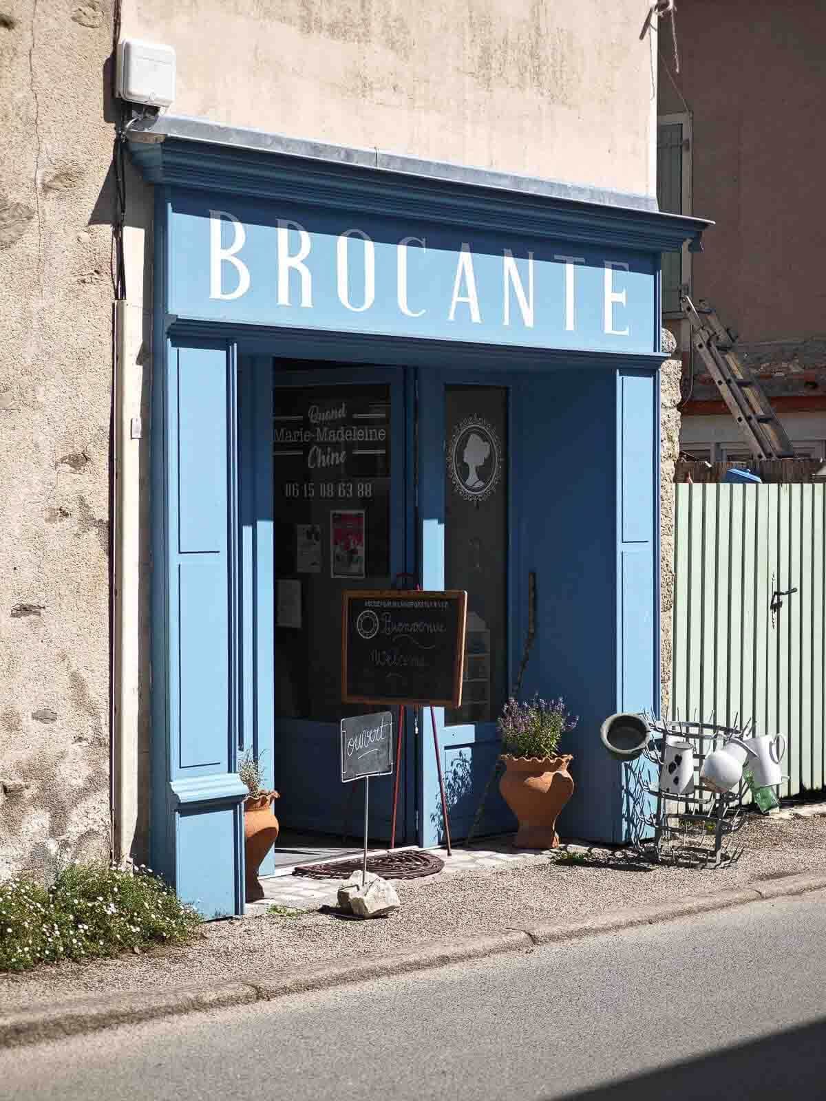 Blue "BROCANTE" shop front with sign, potted plants, and chalk board sign.