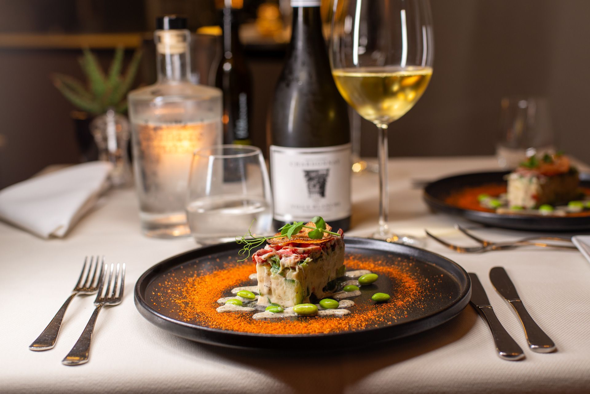Een bord met eten, wijn en bestek staat op tafel. De fles wijn en gin zijn zichtbaar.