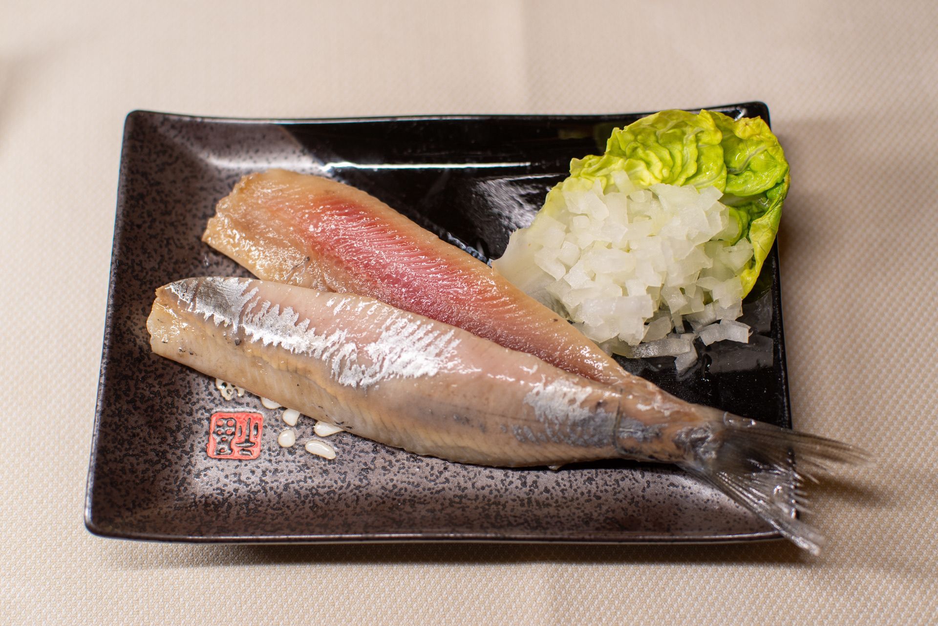 Gezouten haringfilets met ui en sla op een vierkant bord.