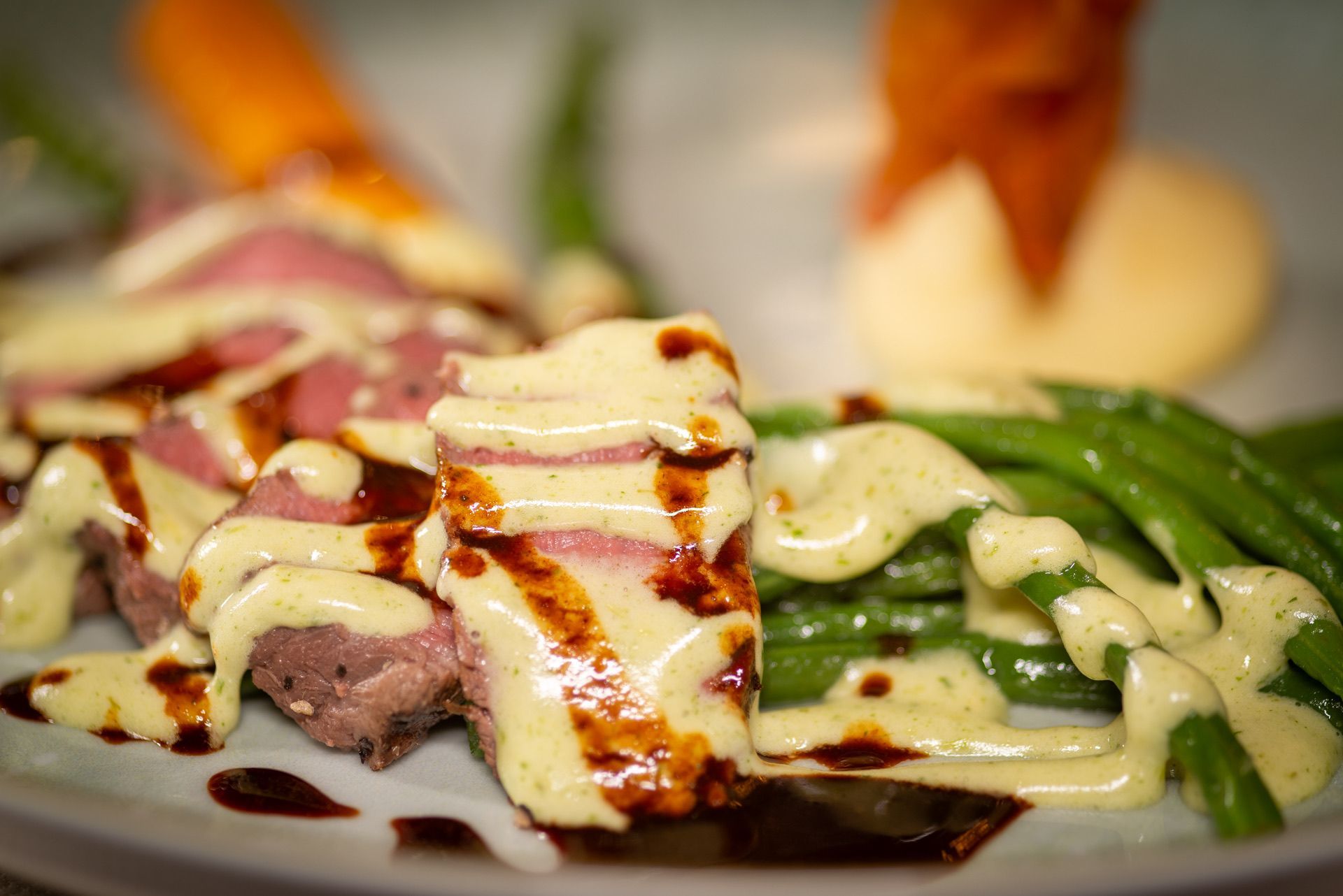 Gesneden vlees met saus, sperziebonen, wortel en aardappel op een bord.