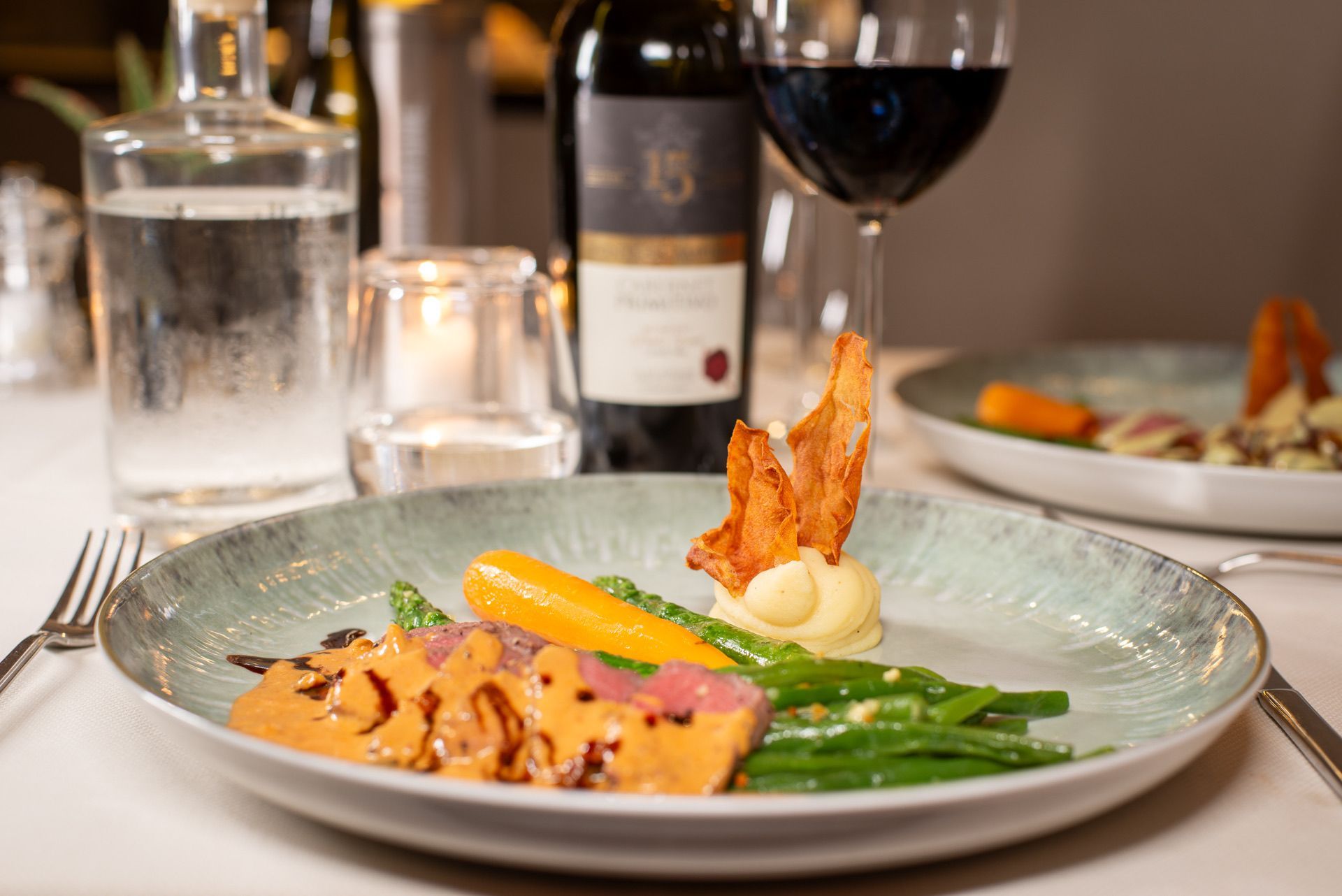 Bord met tonijn, groenten, saus, spek en een glas rode wijn op tafel.