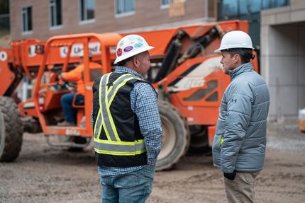 Two construction workers are standing next to each other on a construction site.