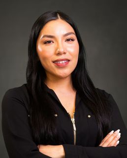 A woman in a black jacket is posing for a picture with her arms crossed.