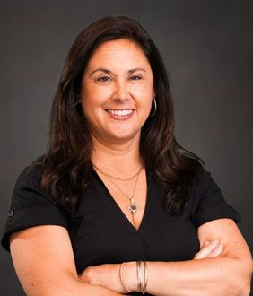 A woman in a black shirt is smiling with her arms crossed.