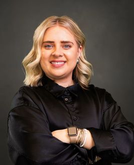 A woman wearing a black shirt and a smart watch is smiling with her arms crossed.