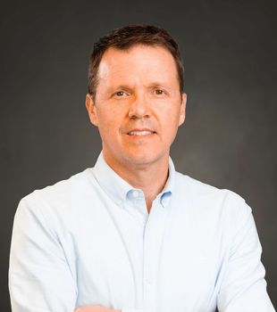 A man in a light blue shirt is standing with his arms crossed.