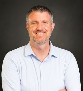 A man with a beard is smiling for the camera with his arms crossed.