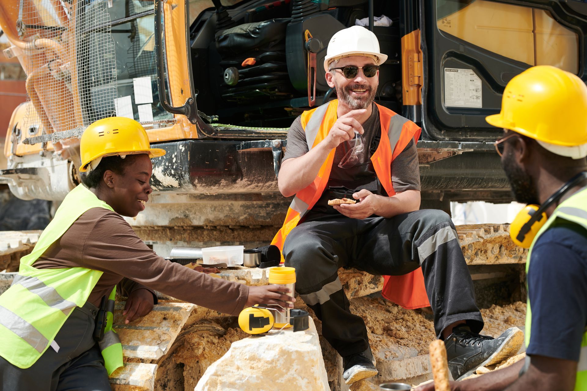 A group of construction workers are sitting on a rock in front of a bulldozer.