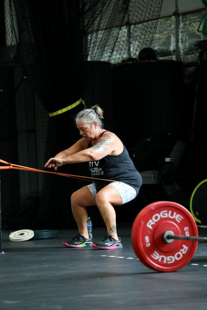 A woman is squatting down next to a barbell in a gym.