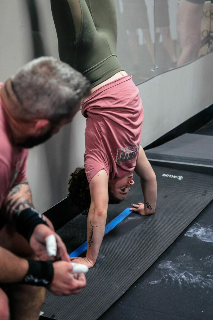 A man is helping a woman do a handstand in a gym.