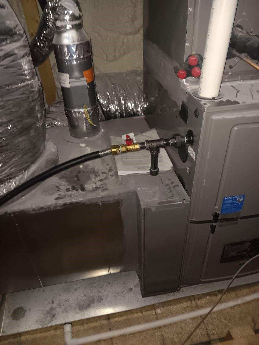 Furnace and ductwork in a utility room. Black gas line with a valve. Grey metal and silver ducting.