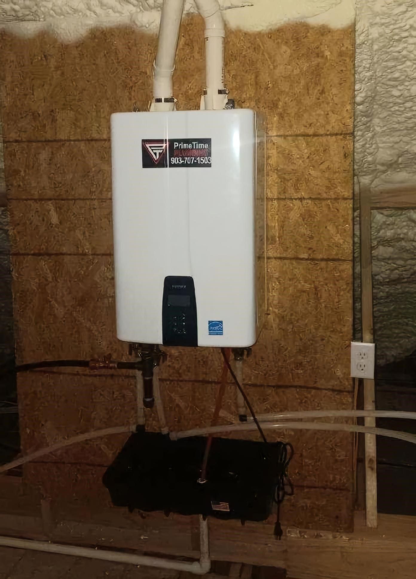 White tankless water heater mounted on a wooden wall, with connected pipes and exhaust vents.
