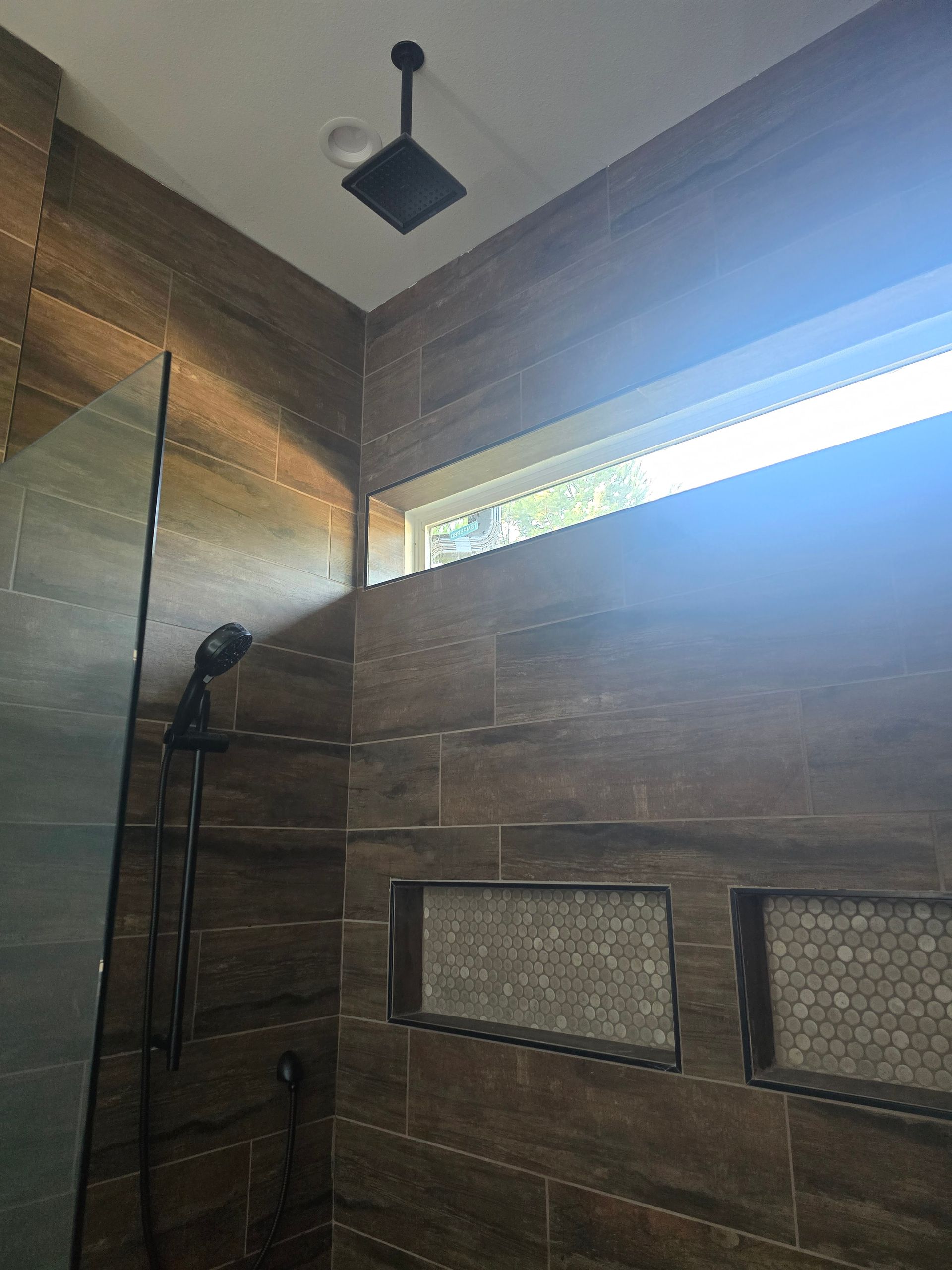 Bathroom shower with brown tiled walls, glass door, and black shower fixtures.