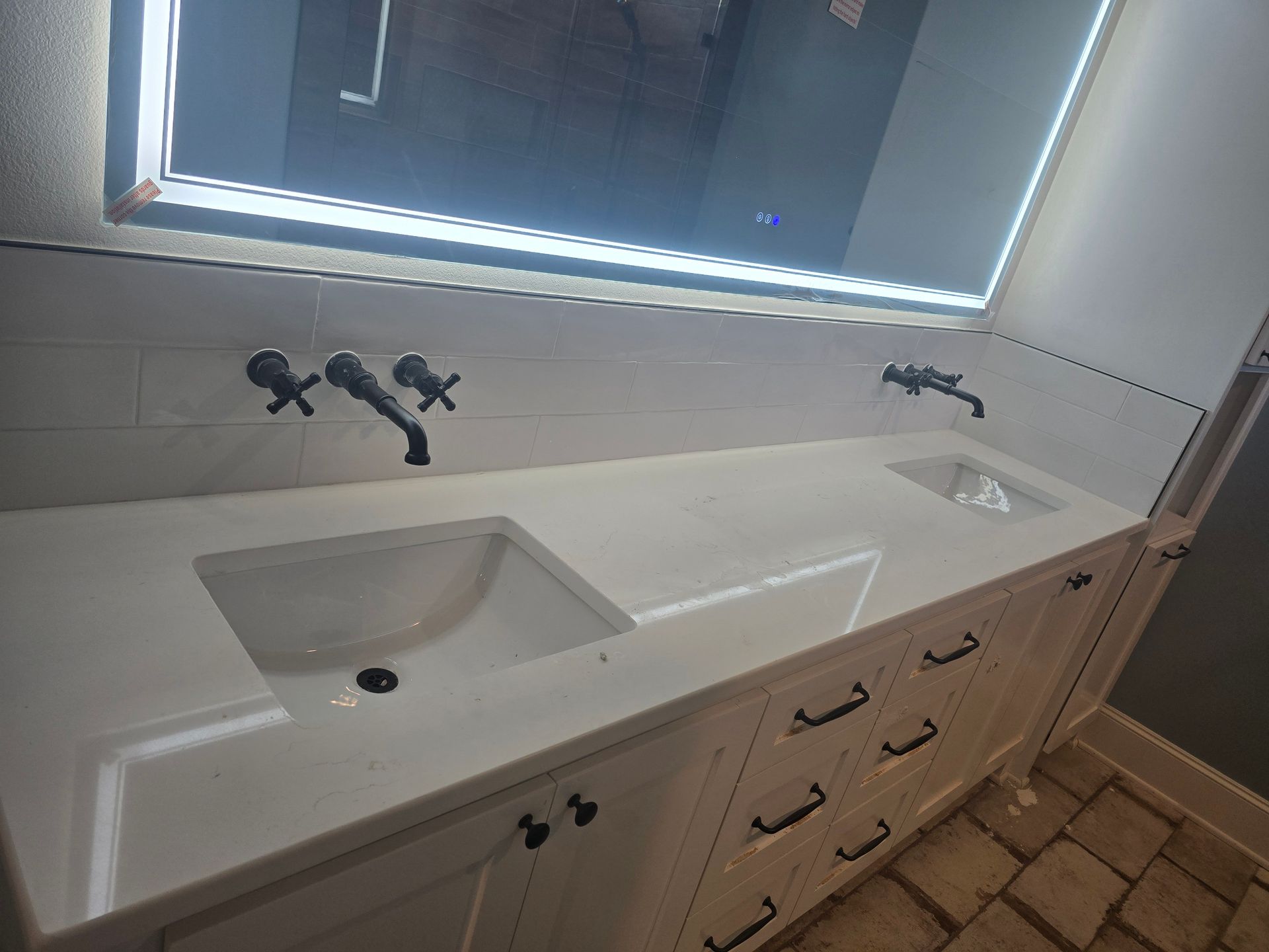 White bathroom vanity with two sinks, black fixtures, and a lighted mirror.