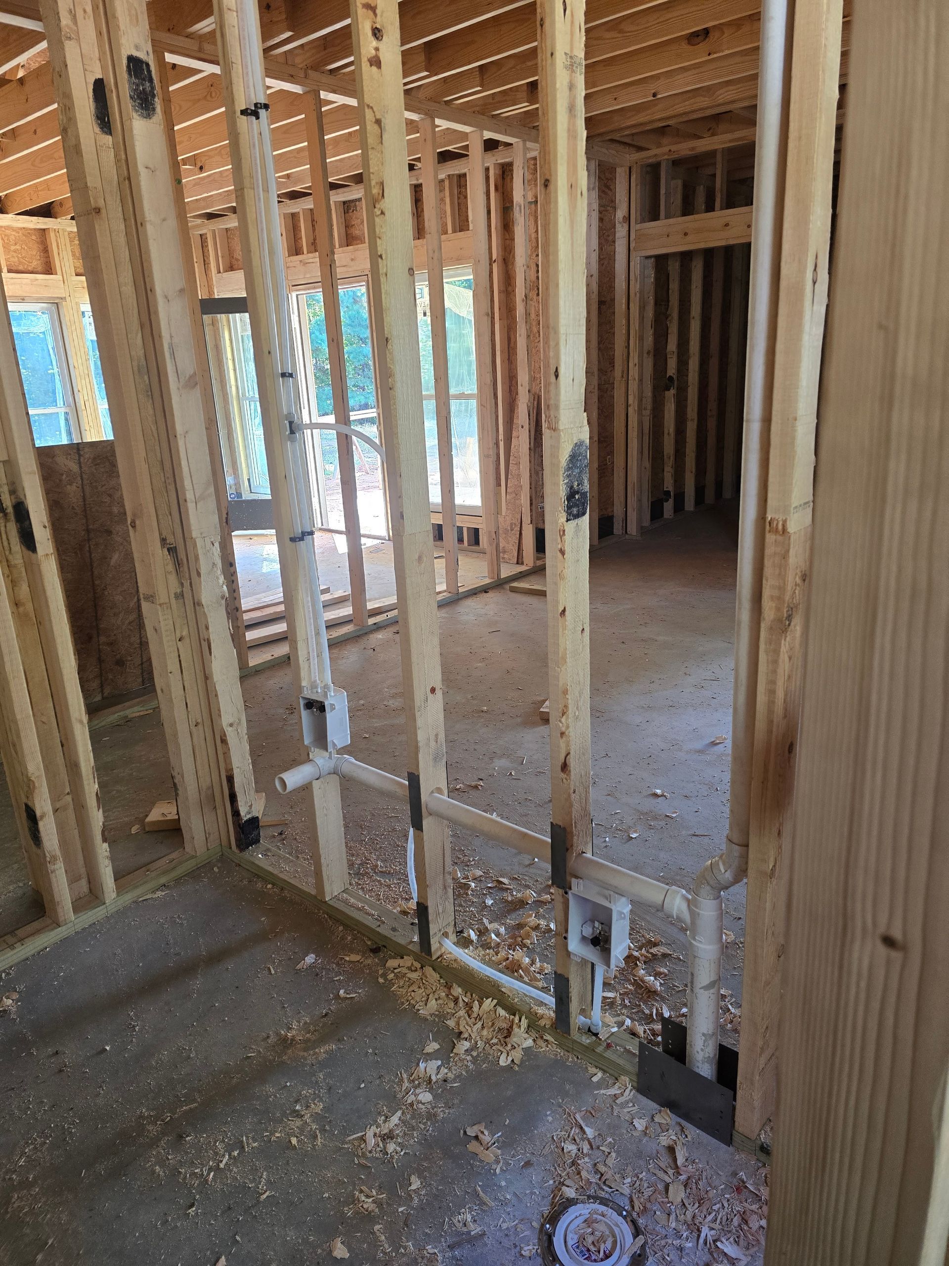 Interior framing of a house under construction; wood studs, pipes, and concrete floor.
