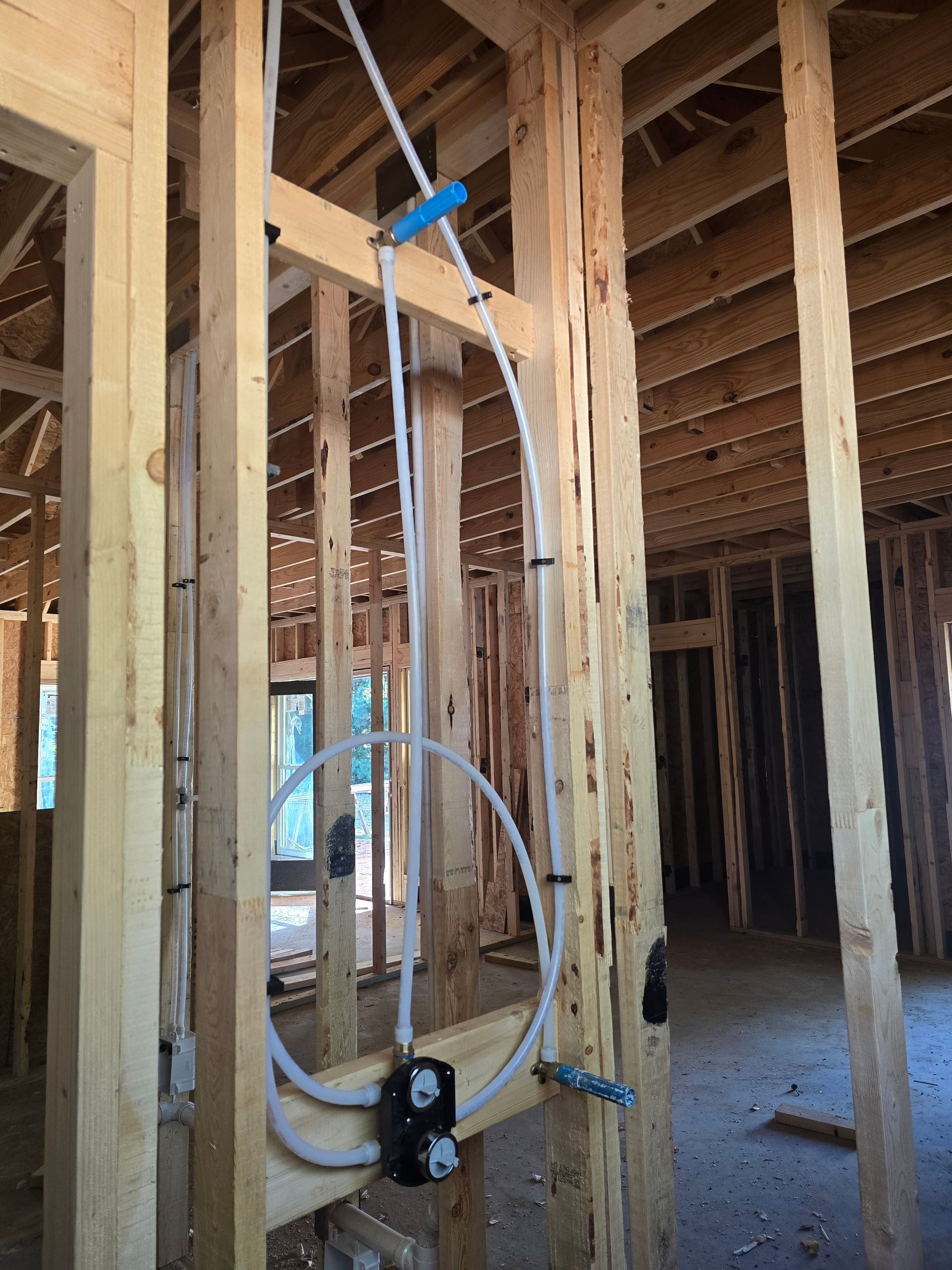 Wooden frame with white pipes and black plumbing fixtures in a new construction setting.