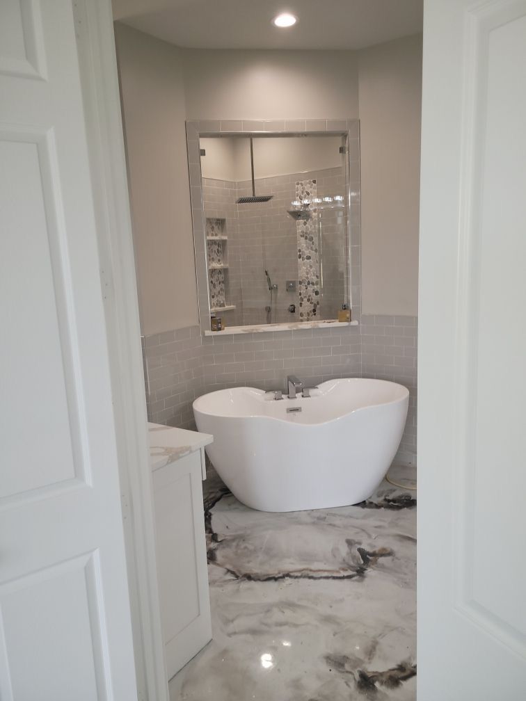 Bathroom with a white freestanding tub, shower, and marble-like flooring.