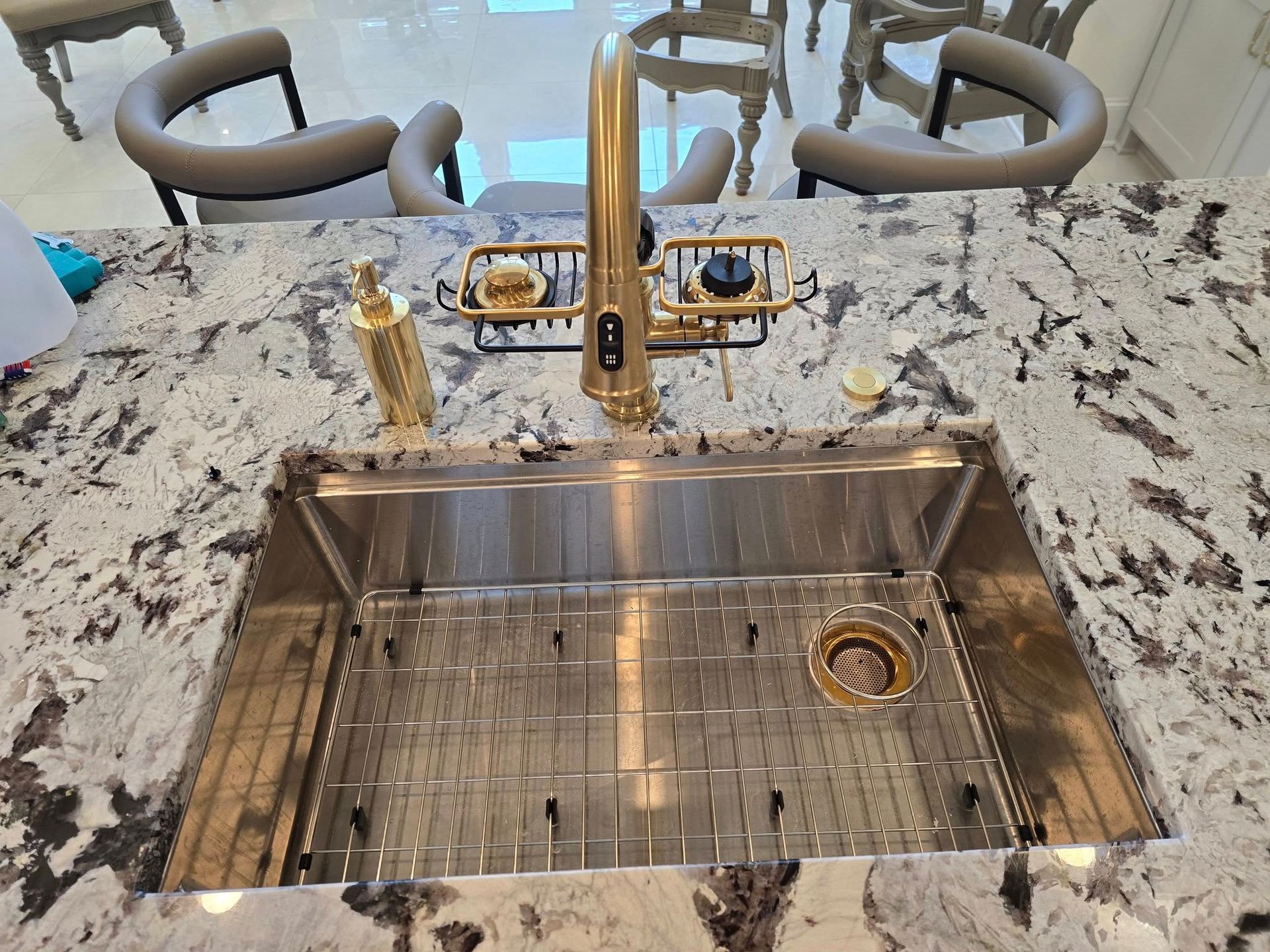 Stainless steel kitchen sink with gold faucet on a granite countertop, with a dish rack and accessories.