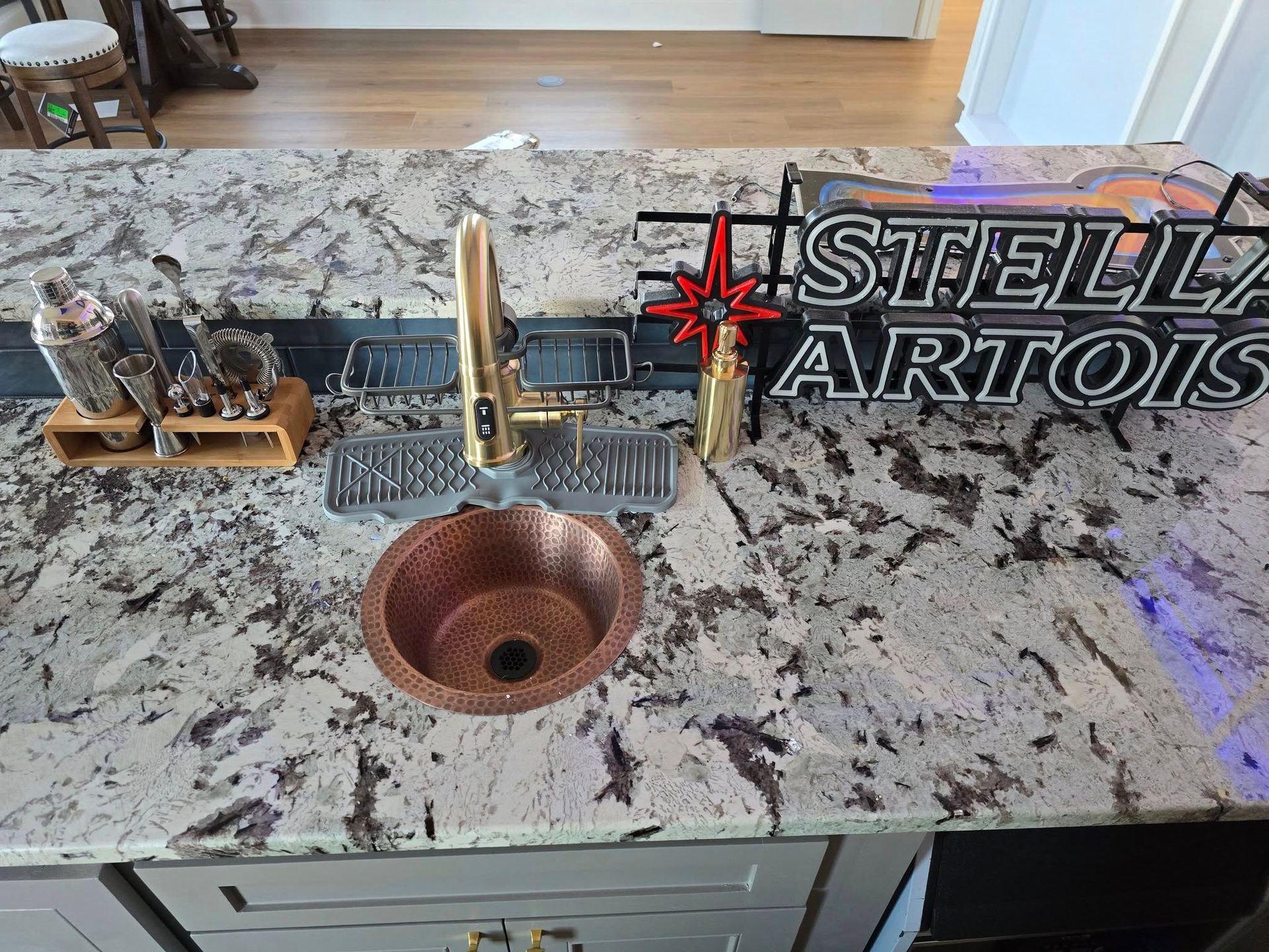 Copper sink with gold faucet on granite countertop, Stella Artois sign behind.