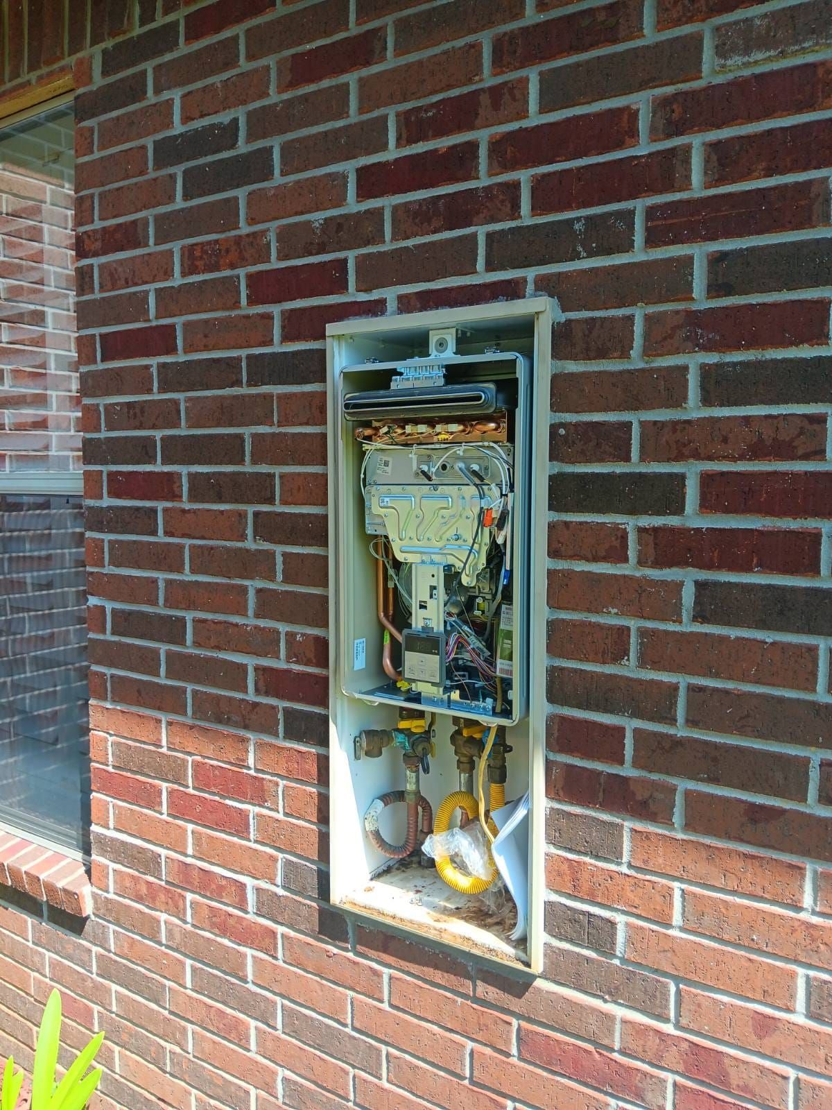 Exterior utility box recessed in a red brick wall, showing wiring and components.