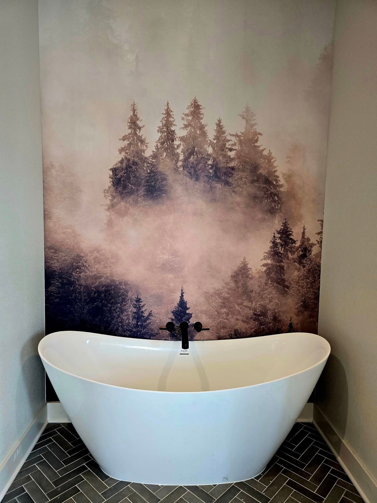 White bathtub in front of a forest mural with a black faucet. Dark gray tiled floor.