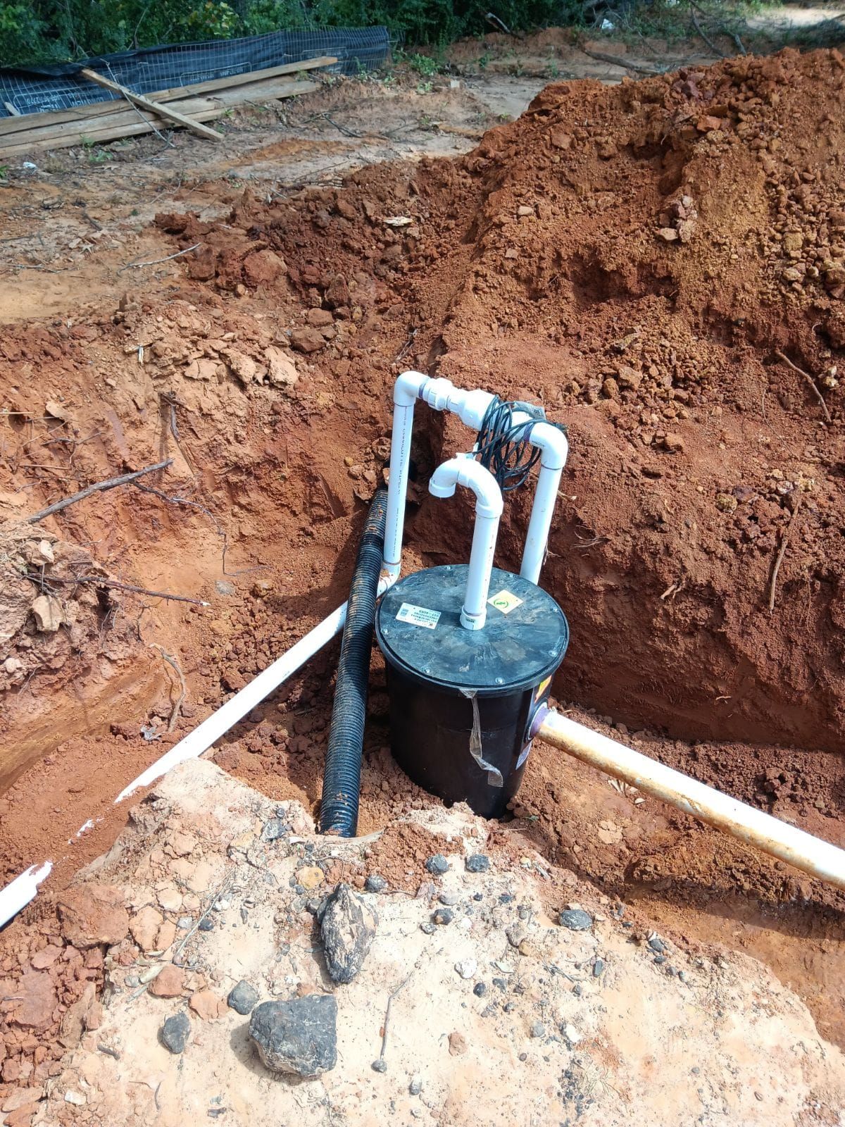A black pump in a hole, with white pipes, surrounded by dirt and soil.