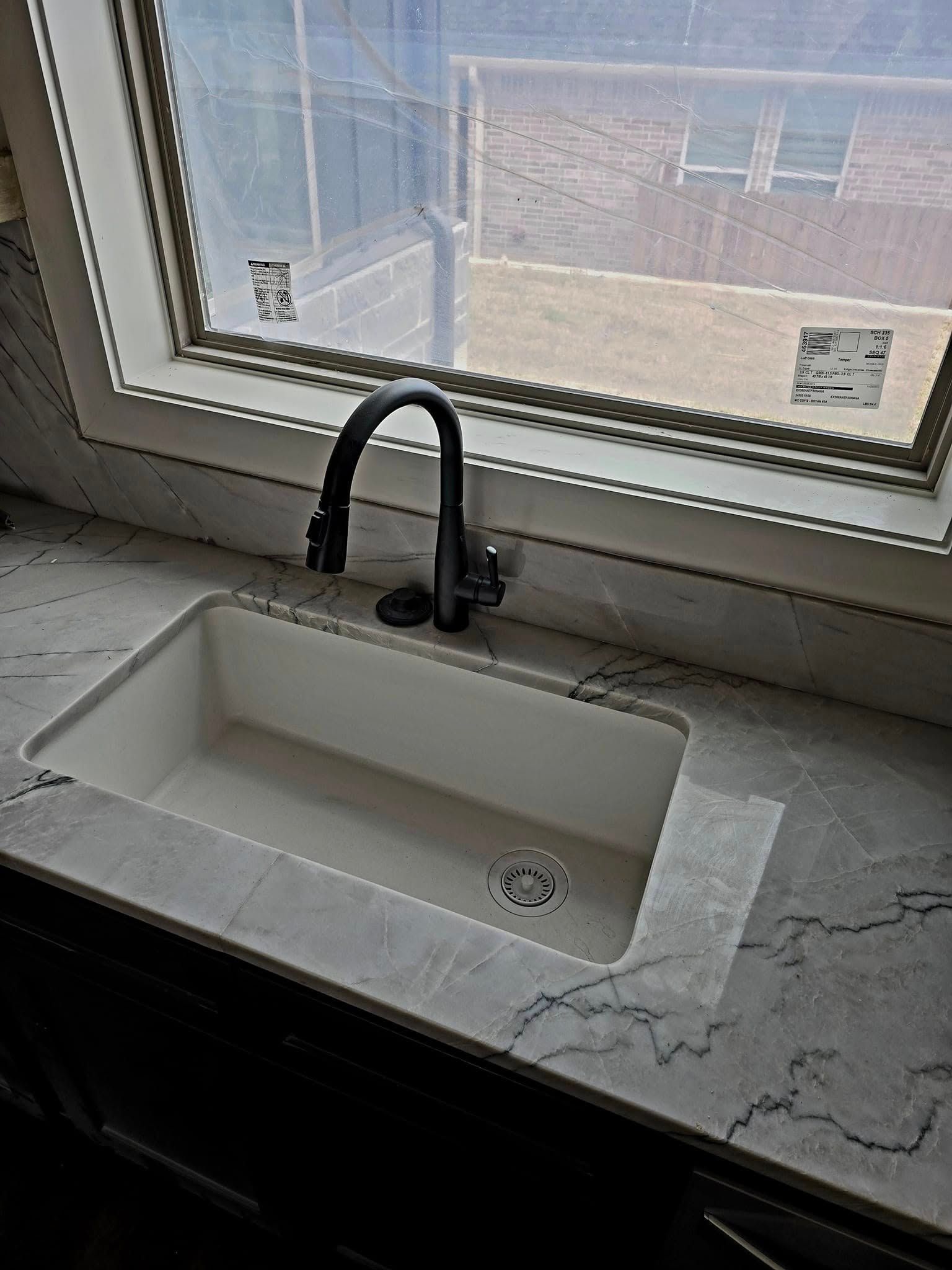 Kitchen sink with black faucet, white sink basin, and gray countertop, near window.