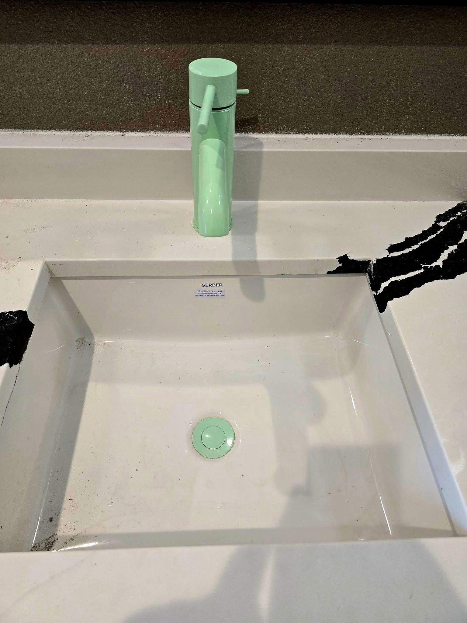 Light green faucet over a white rectangular sink with black paint splatters.
