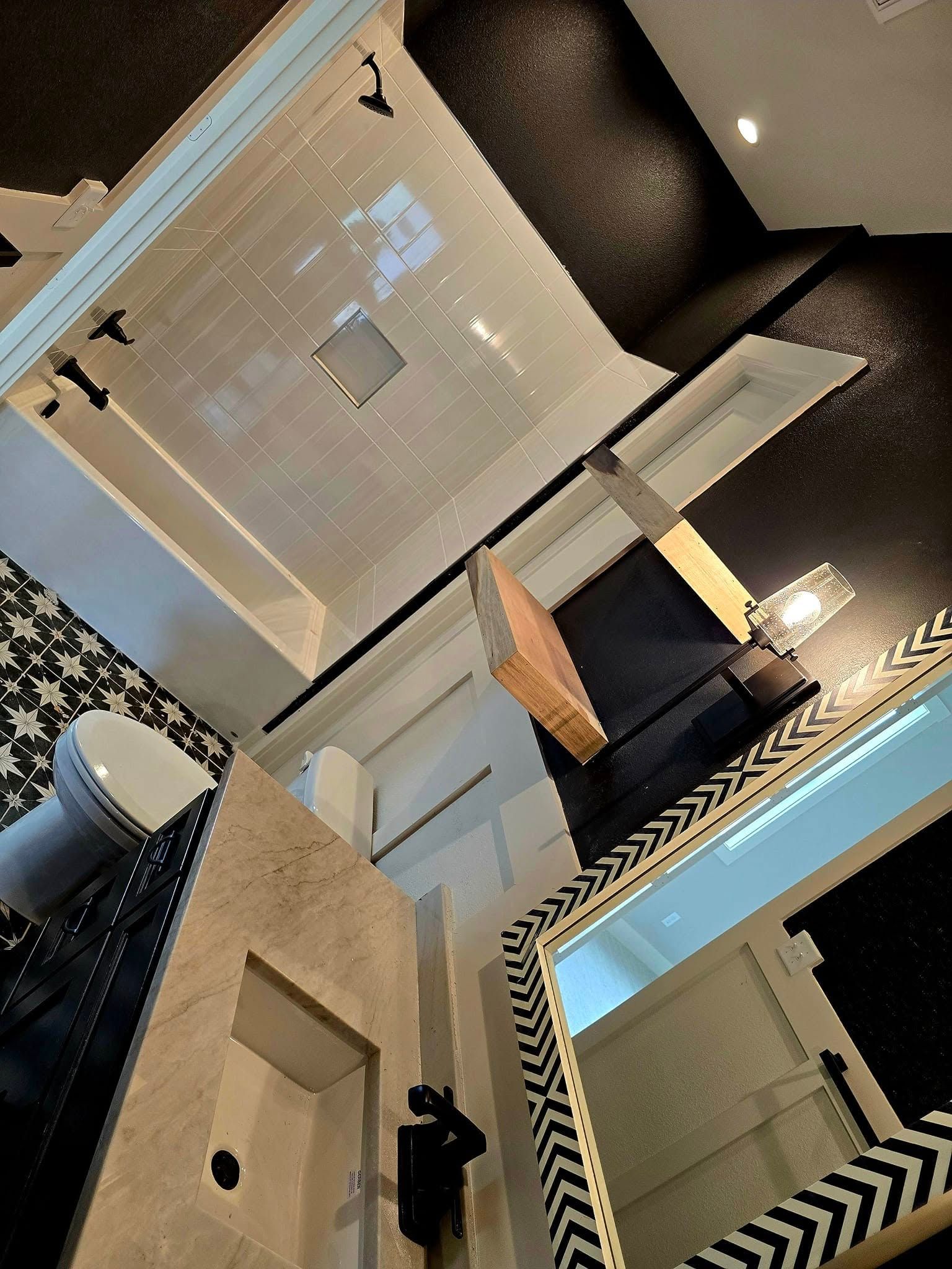 Bathroom with black and white patterned floor, white tiled shower, and mirror.