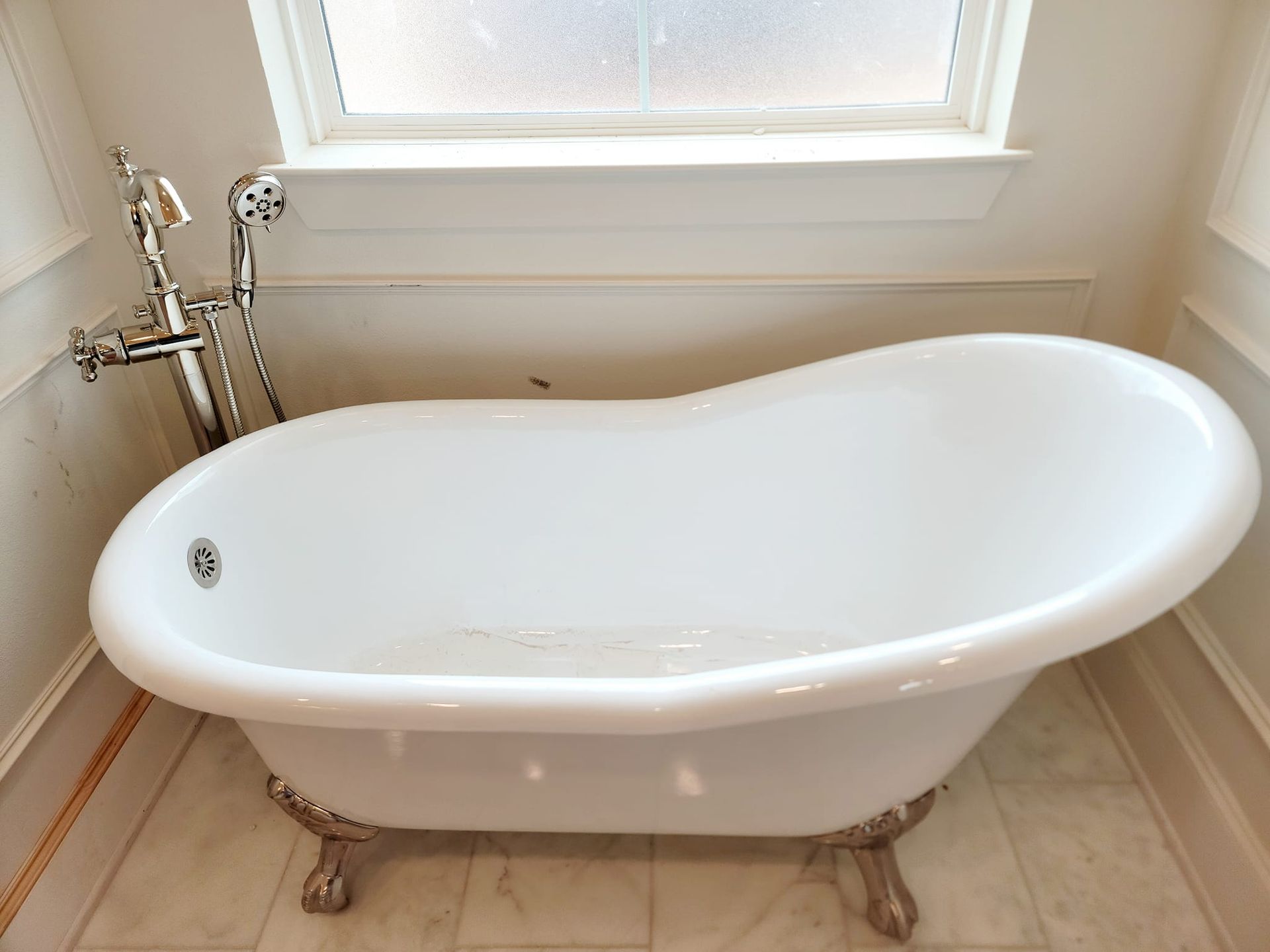 White clawfoot bathtub in bathroom with silver faucet fixtures, under a window.