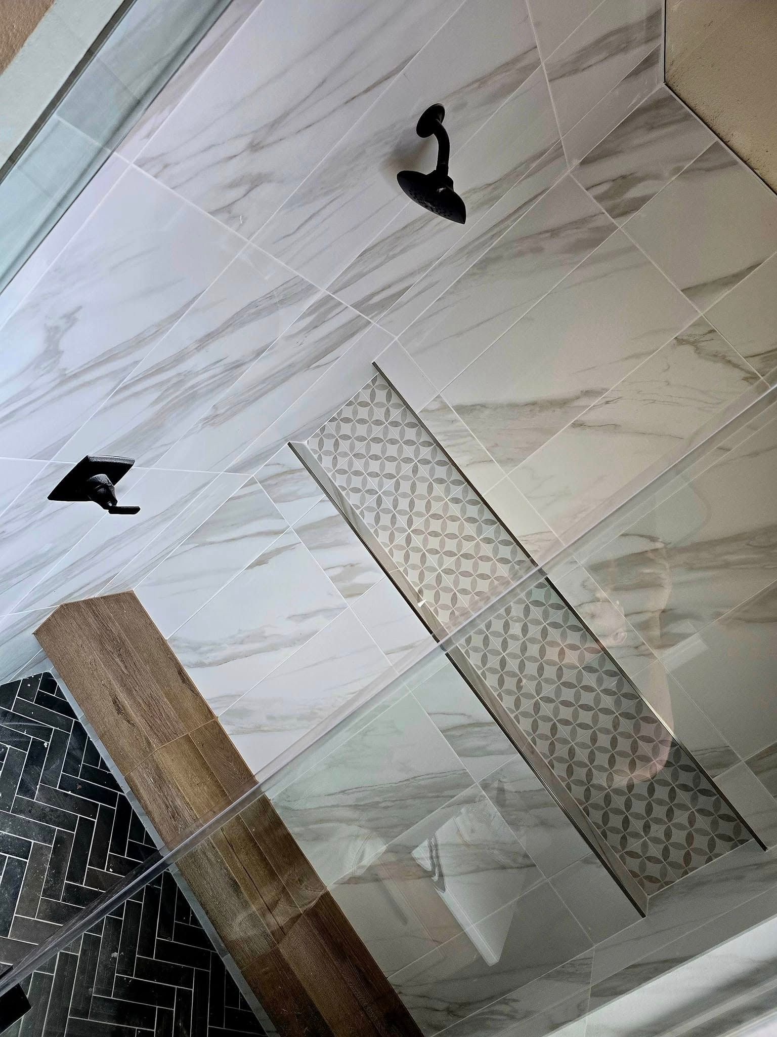 Shower with patterned tile floor, dark fixtures. Decorative tile insert and wood-look tile.