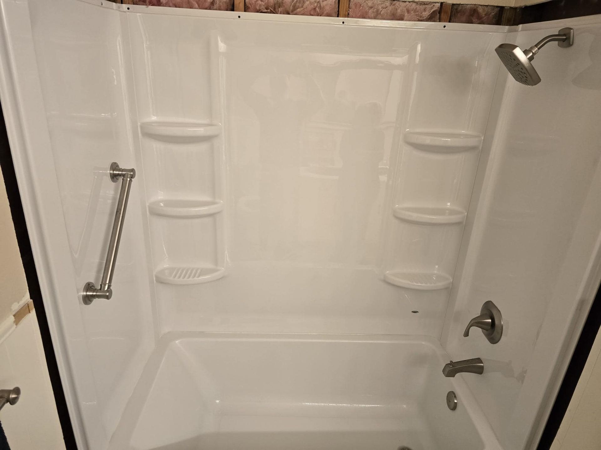 White bathtub and shower combo with built-in shelves, grab bar, and showerhead.