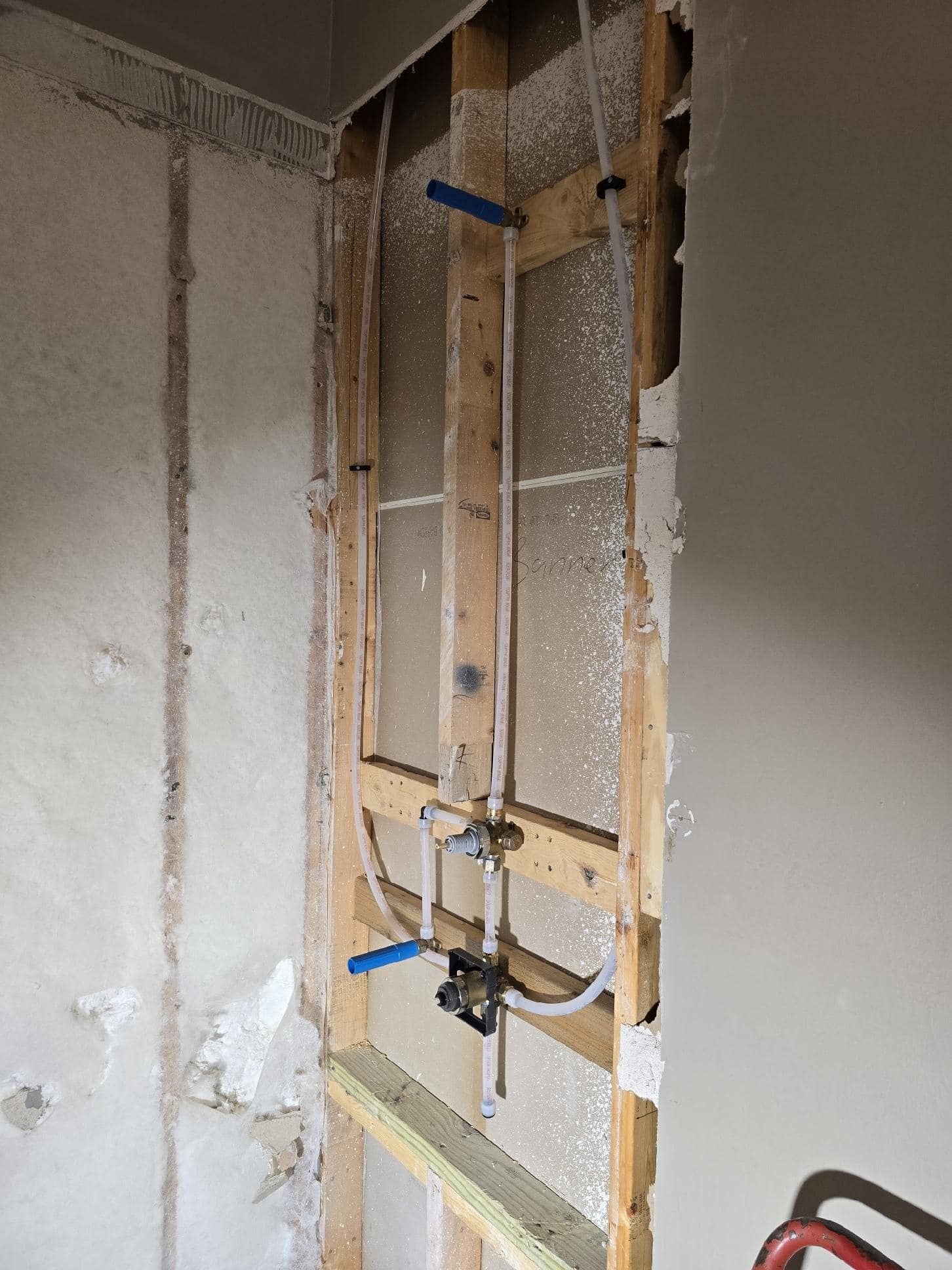 Framed wall cavity with plumbing pipes and valves visible, prepared for shower fixtures.