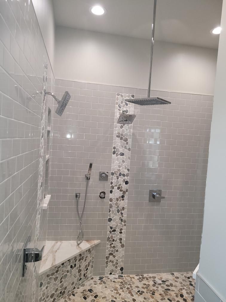 Shower with gray tile walls, pebble floor, built-in bench, and multiple showerheads.