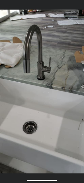 A new stainless steel kitchen faucet over a white farmhouse sink on a marble countertop.