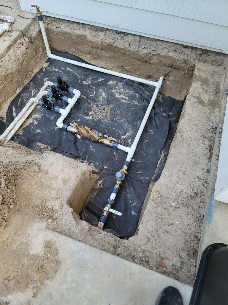 Irrigation system components in an excavated pit, including pipes, valves, and a backflow preventer.