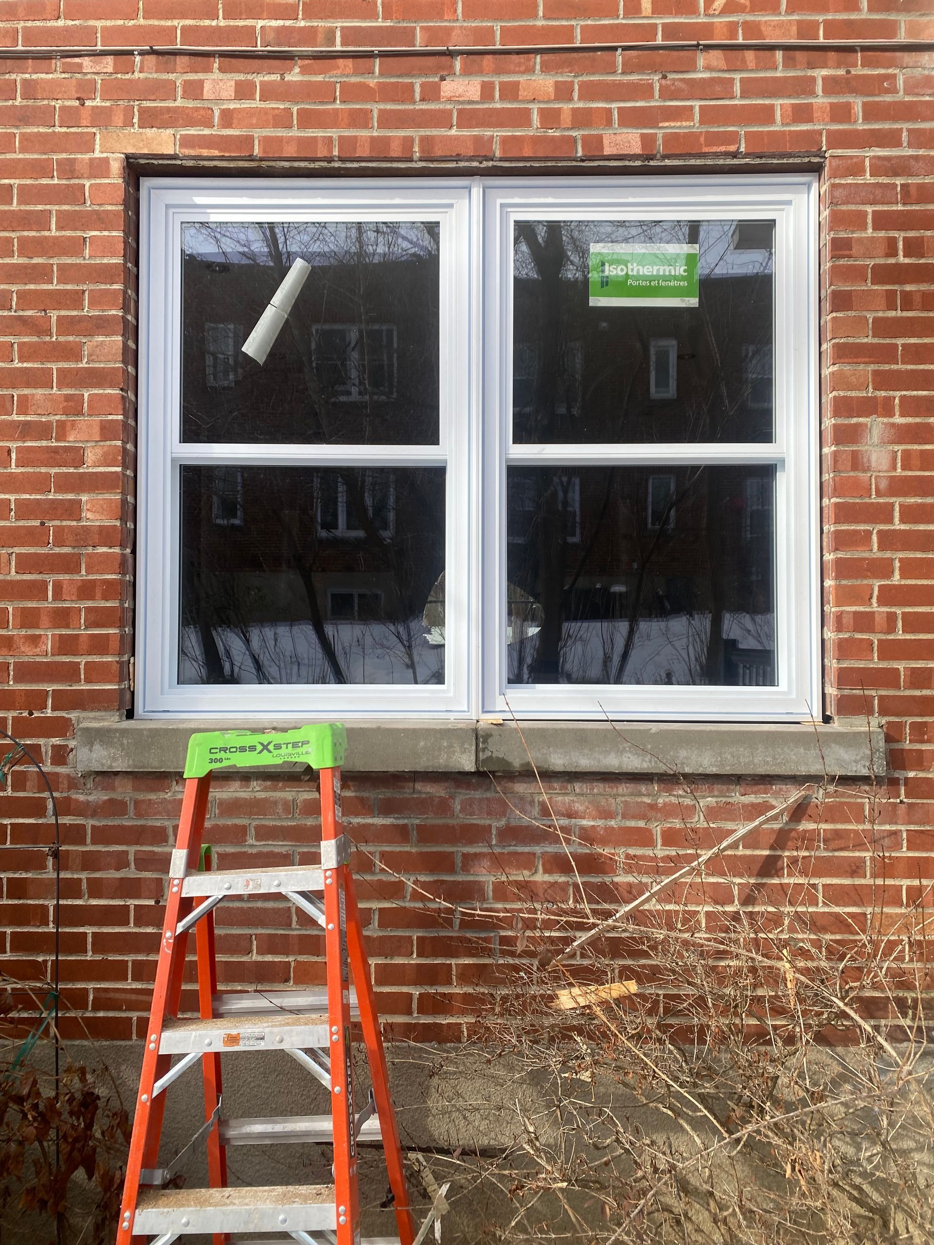 Fenêtre à guillotine blanche dans un immeuble en briques rouges avec une échelle orange en dessous.