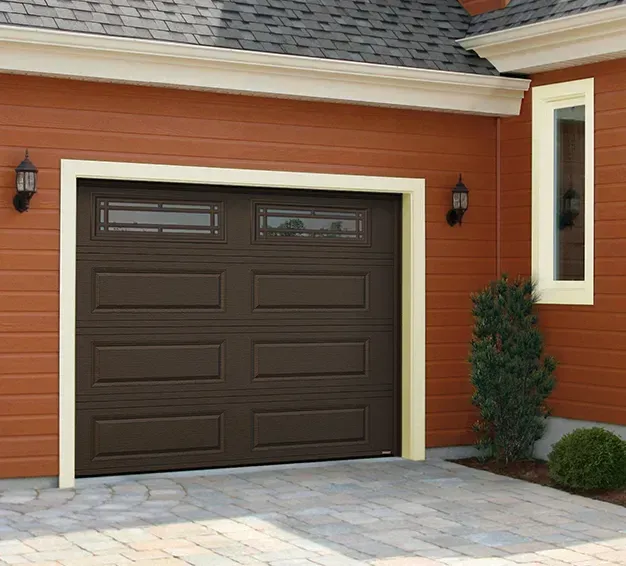 Porte de garage marron sur une maison orange, avec allée en briques et petits buissons.