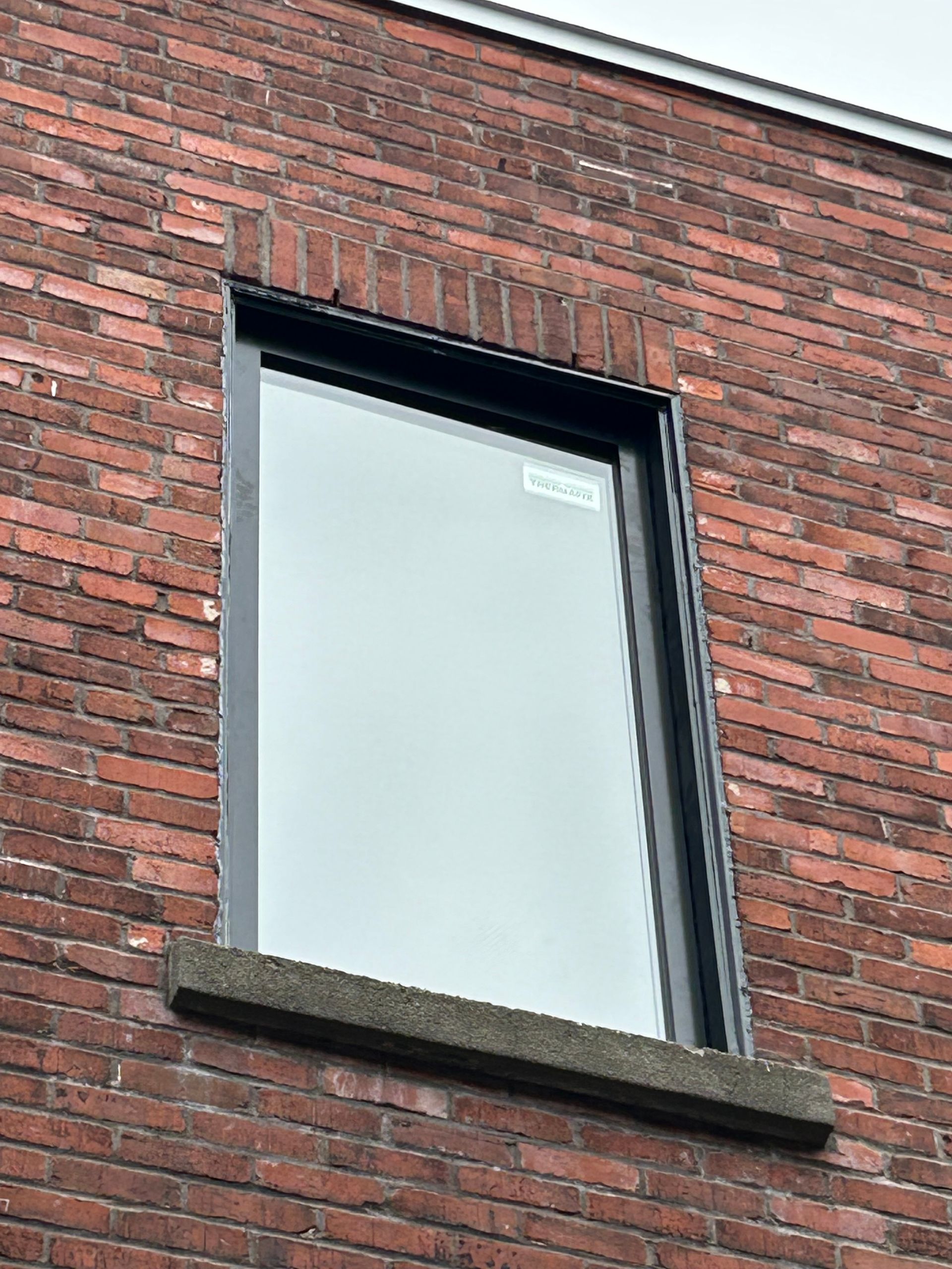 Façade en briques avec une fenêtre à cadre sombre. La fenêtre repose sur un appui en béton.