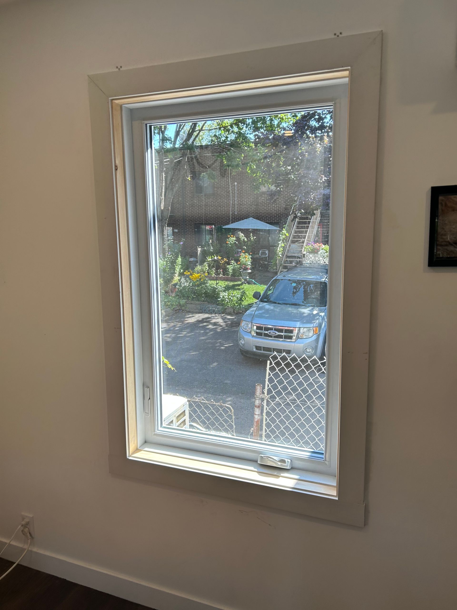 Fenêtre avec cadre blanc, donnant sur une allée, une voiture et une cour.