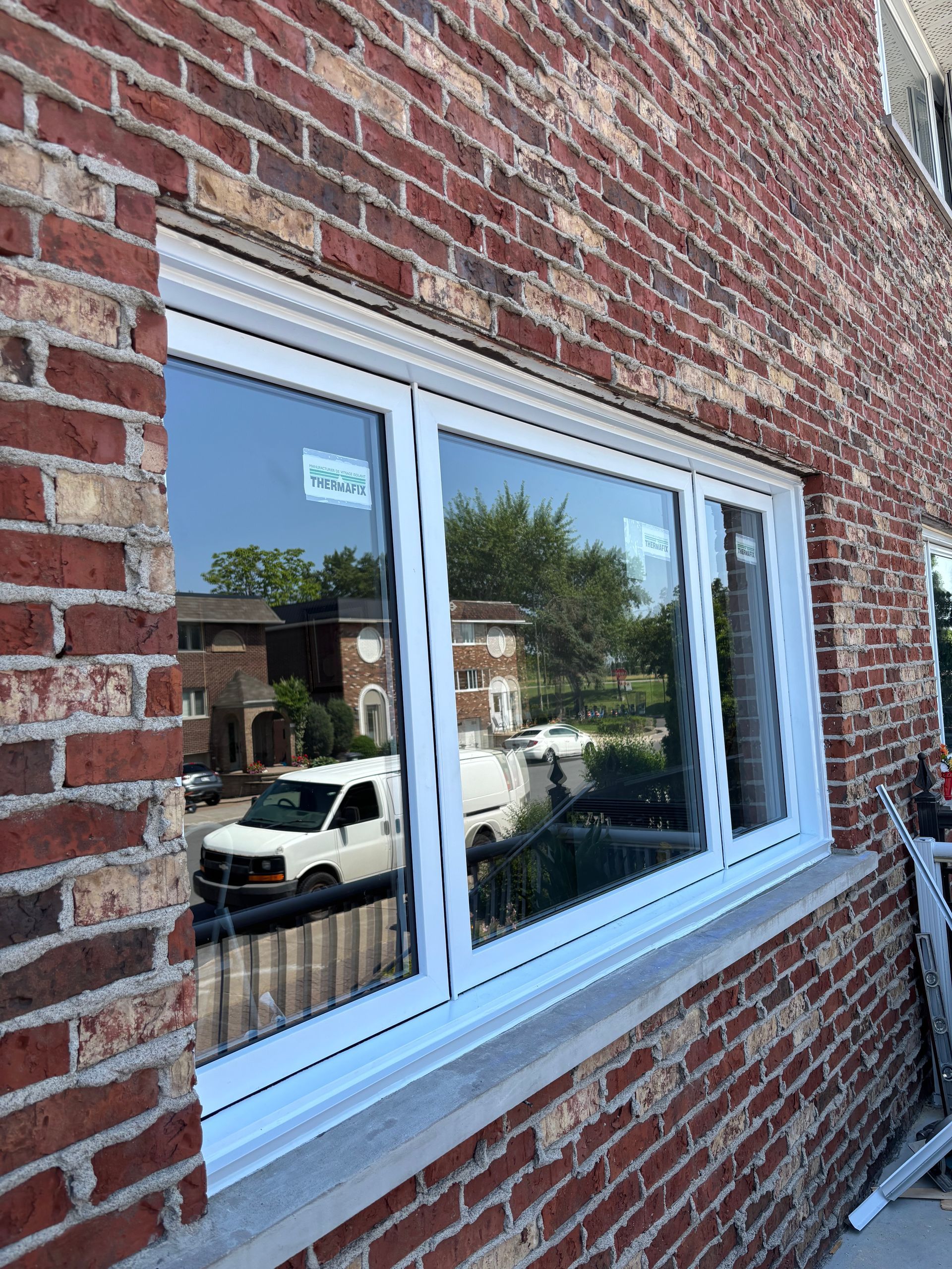 Une fenêtre blanche est en cours d'installation sur un bâtiment en briques.