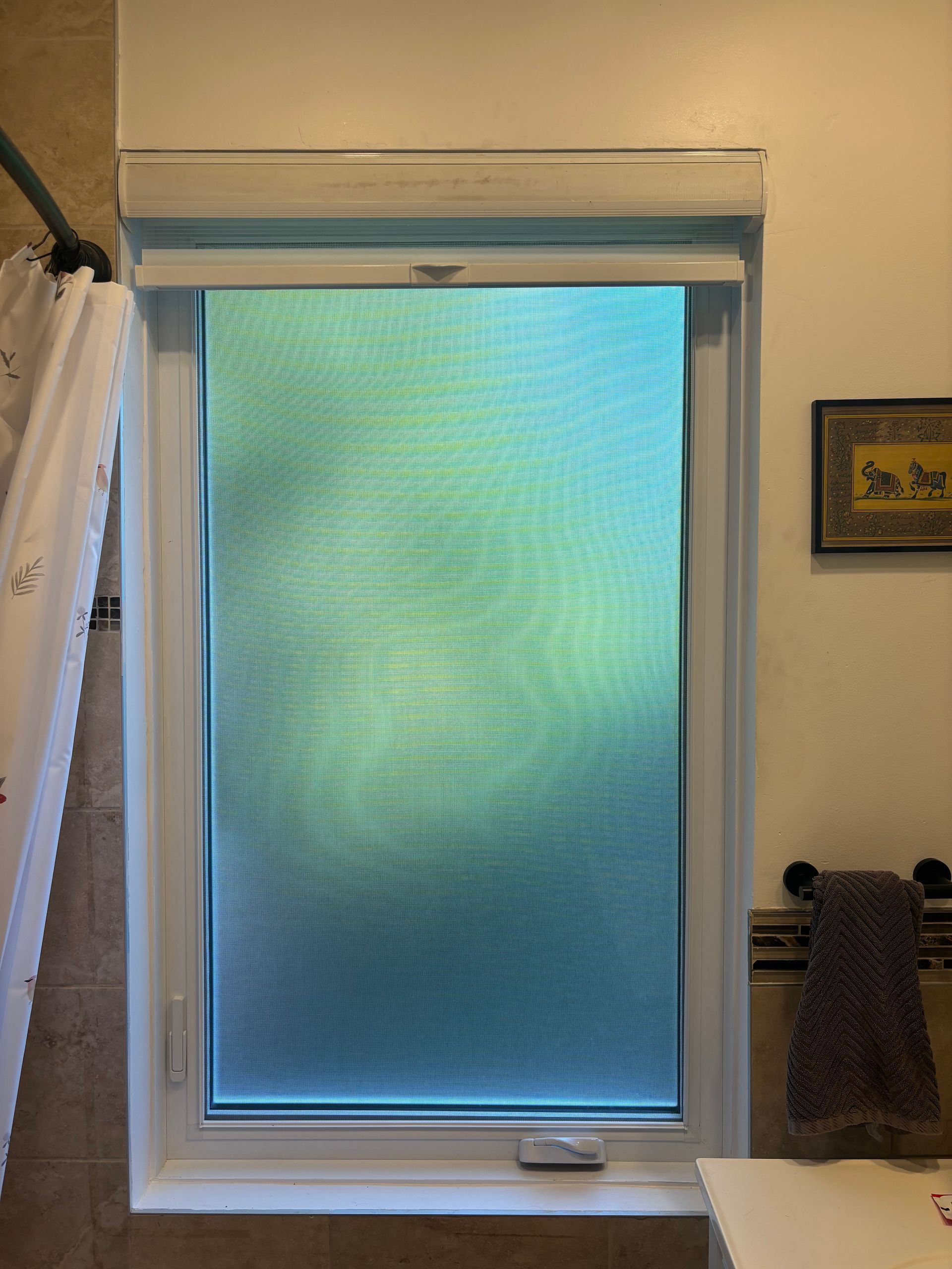 Une fenêtre de salle de bain avec un store cellulaire fermé, un cadre blanc et un rideau de douche partiellement