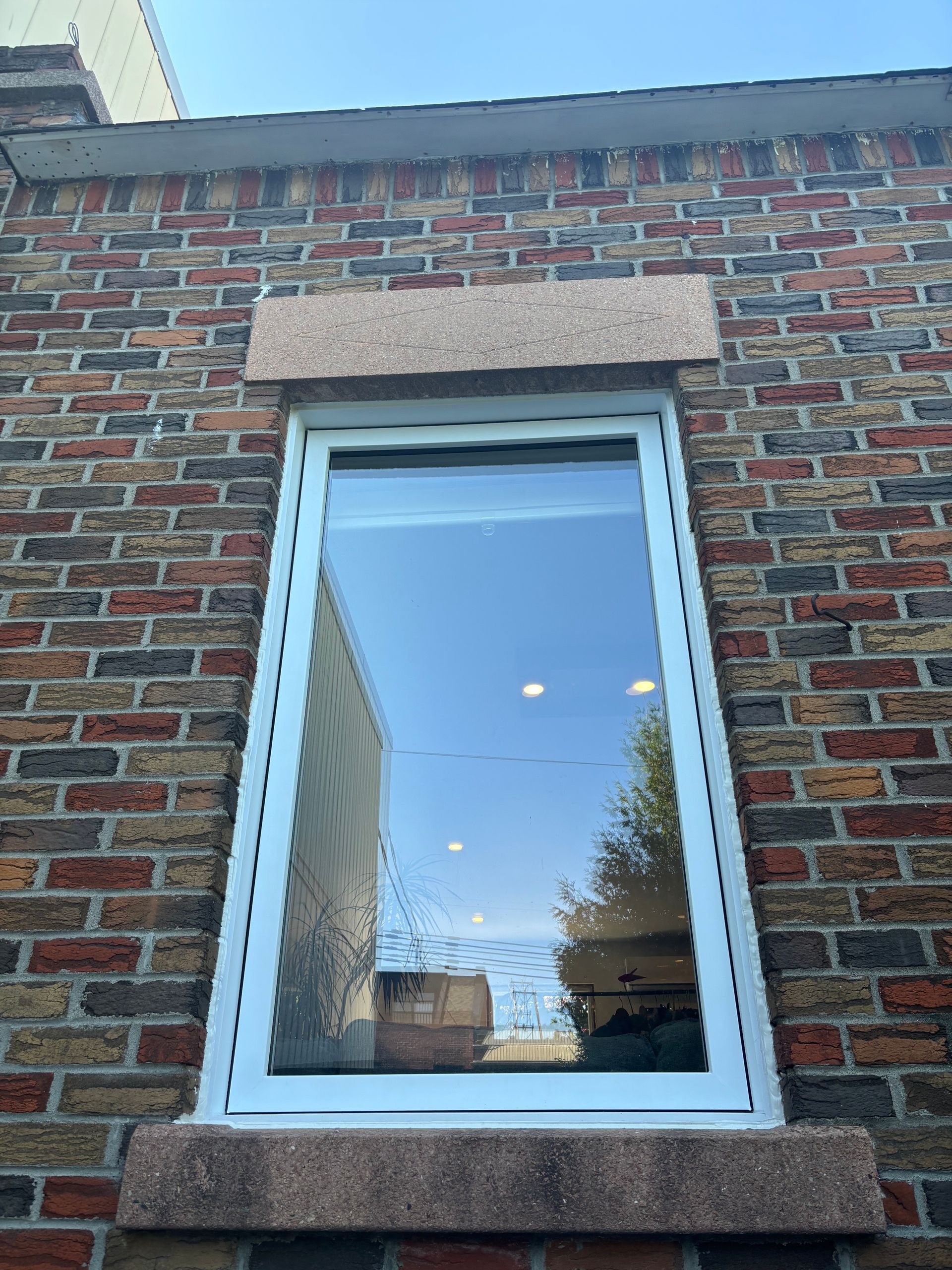 Façade en briques avec une fenêtre à cadre blanc et un linteau en pierre. 