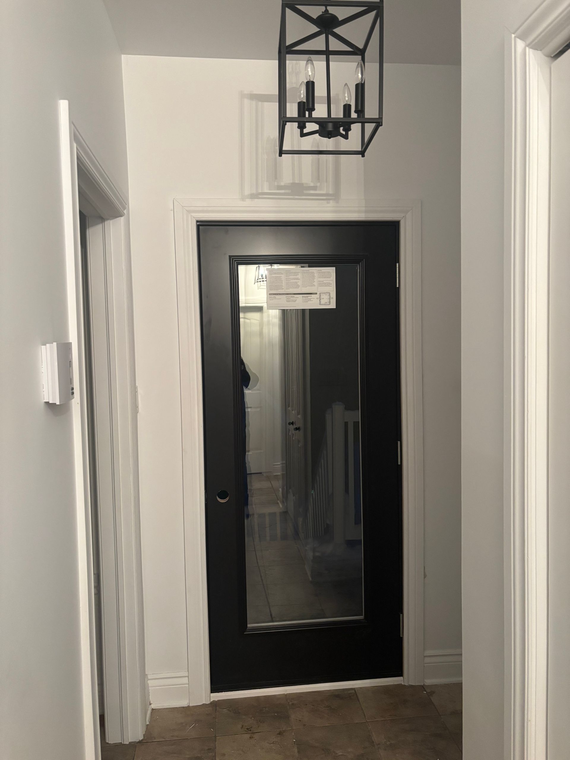 Couloir avec porte noire, luminaire et murs blancs.