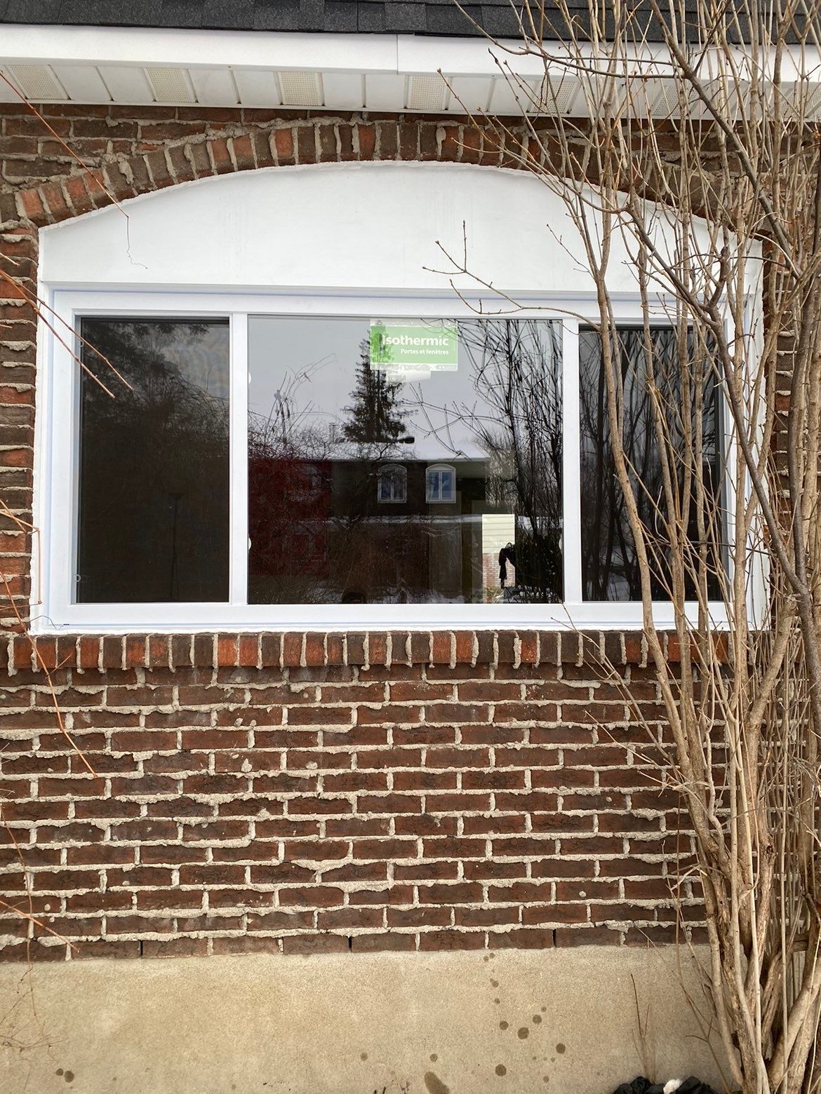 Maison en briques avec une fenêtre rectangulaire encadrée de blanc, surmontée d'une corniche cintrée blanche.