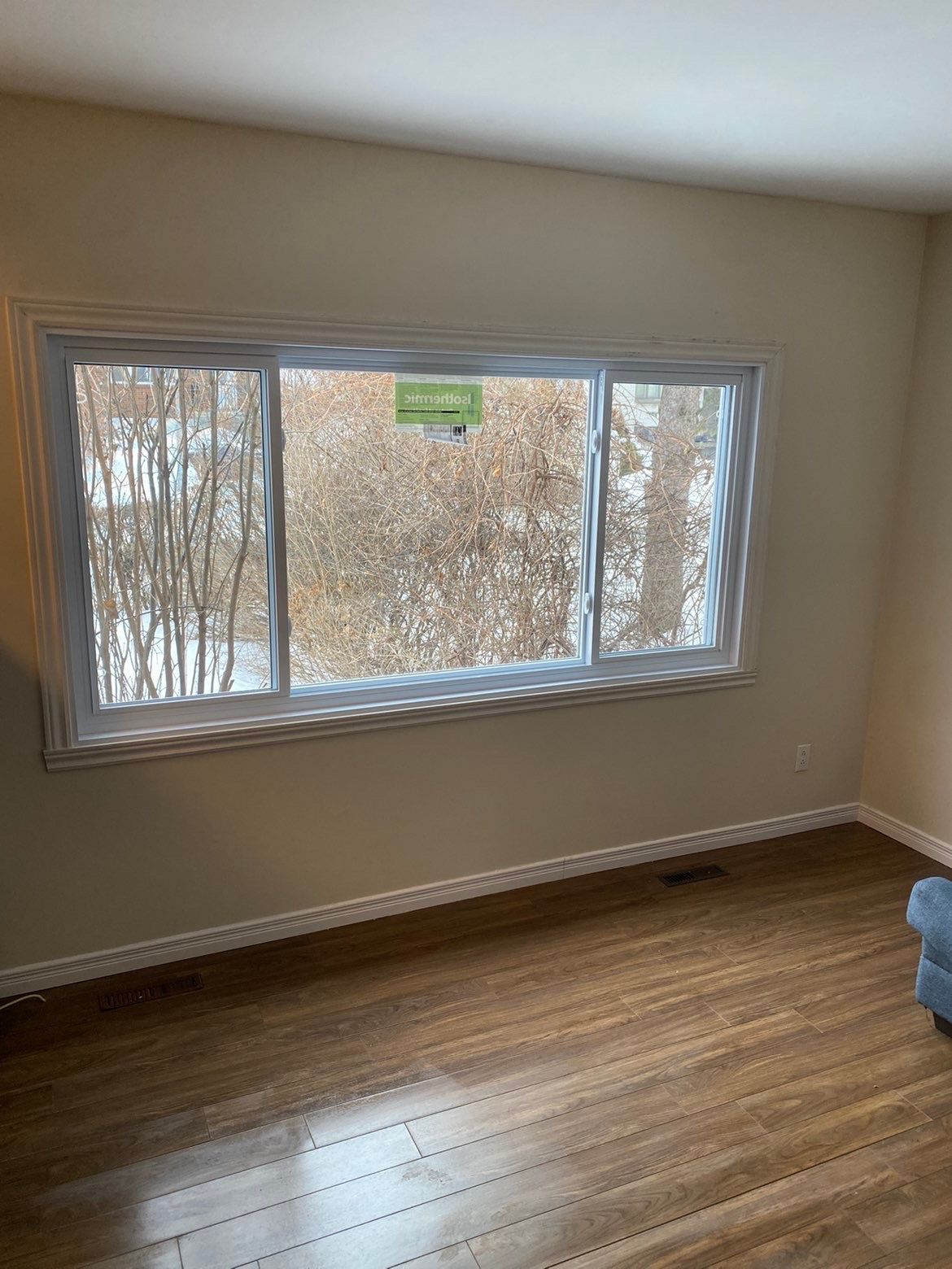 Fenêtre dans une pièce au parquet, donnant sur une zone boisée enneigée.