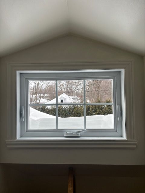 Une fenêtre avec vue sur un champ enneigé et une maison en arrière-plan.