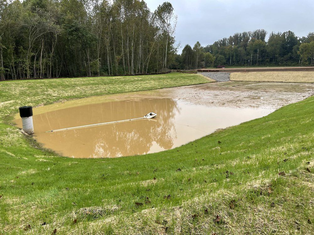 A small boat is floating in a muddy pond in the middle of a grassy field.