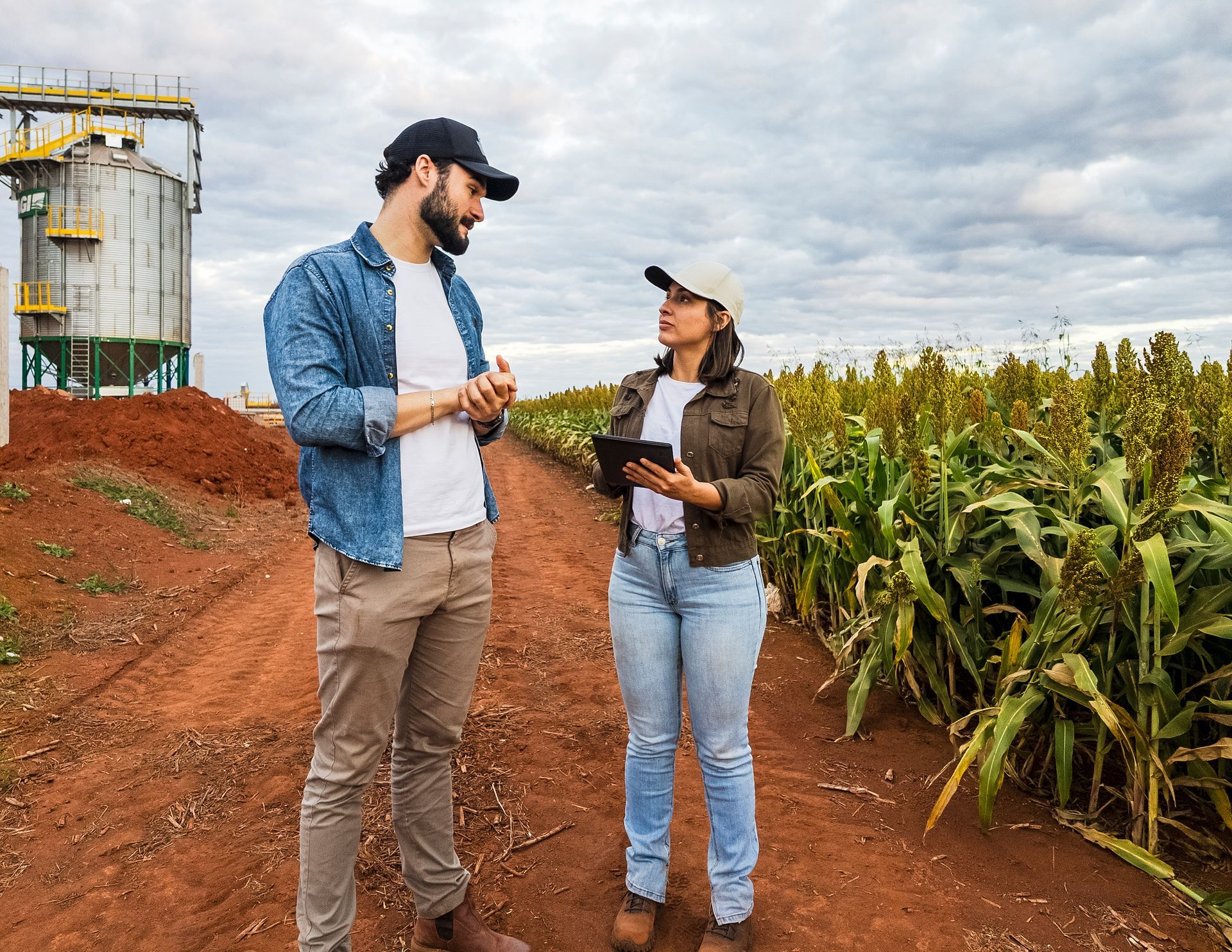 A man and a woman walk through a field. The woman holds a tablet indicating agricultural data collection.