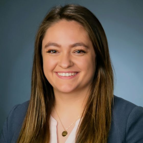 A woman in a suit and necklace is smiling for the camera.